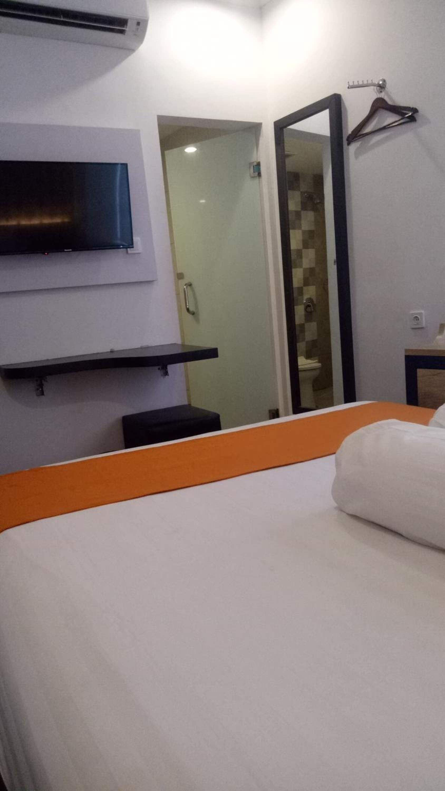 A hotel room with a bed, a TV mounted on the wall, a mirror, and a shower area.