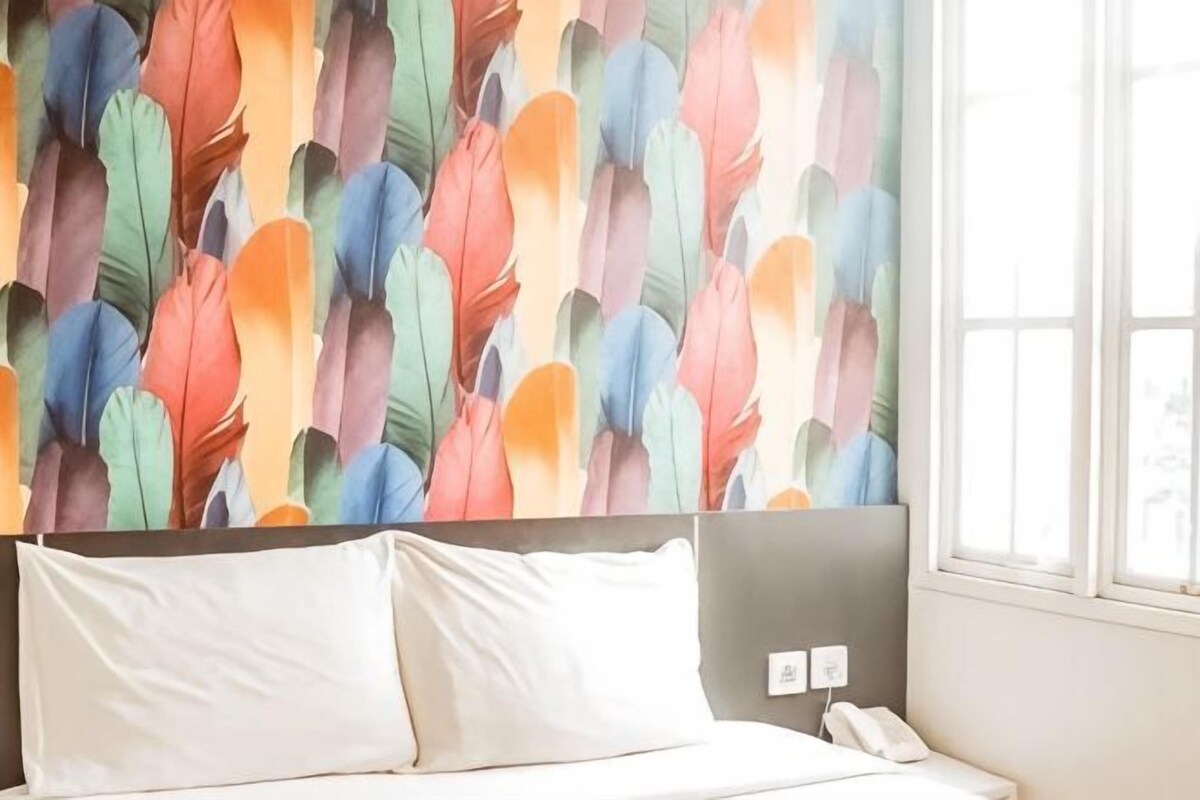 A bed with white linens, a headboard, and a wall with a feather pattern.