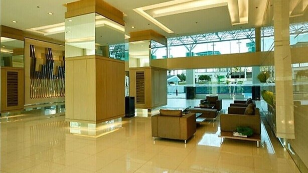 Eine geräumige Lobby mit hoher Decke, moderner Einrichtung und großen Fenstern, die viel Tageslicht hereinlassen.