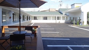 A hotel courtyard with a covered seating area, a parking lot, and a row of rooms with large windows.