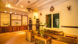 Un salón amplio con un sofá grande, una mesa de centro y una chimenea. Hay objetos decorativos en la repisa y un ventanal con vistas.