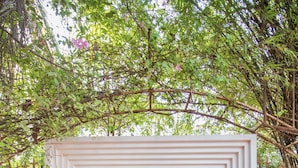 Una entrada de jardín con un arco blanco, plantas en macetas y esculturas de piedra.