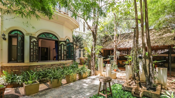 Un patio con plantas en macetas, un taburete de madera y una estructura con techo de paja.