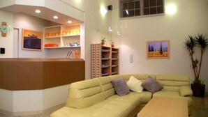 A reception area with a beige sofa, a reception desk, shelves with various items, and a painting on the wall.