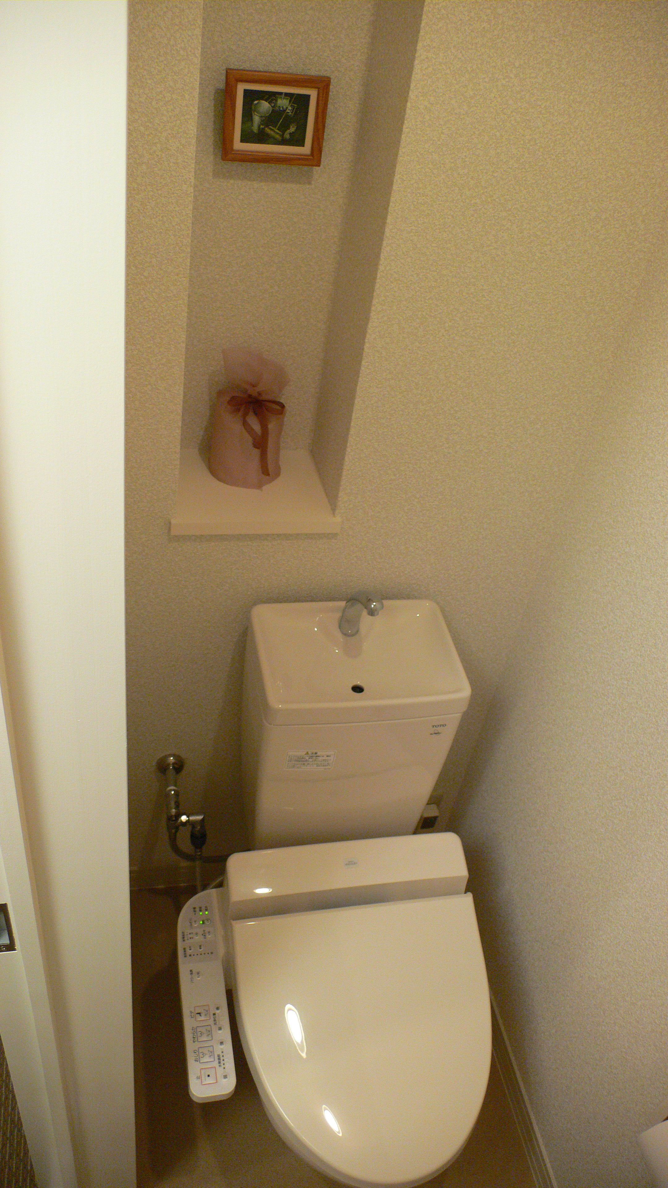 A small bathroom with a toilet, a bidet, and a wall-mounted shelf with a picture.