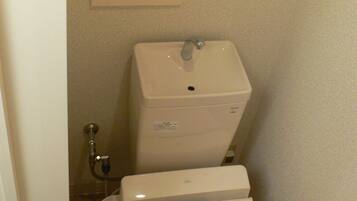 A small bathroom with a toilet, a bidet, and a wall-mounted shelf with a picture.