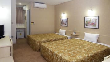 A hotel room with two single beds, a desk with a computer, an air conditioning unit, and two wall-mounted light fixtures.
