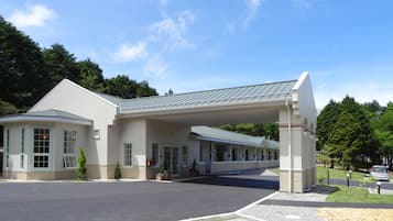 A modern building with a covered entrance, large windows, and a parking area.