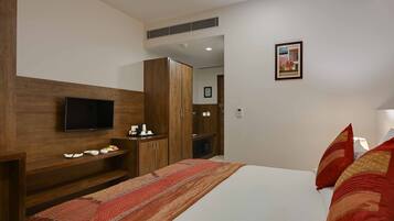 A hotel room with a bed, a TV, wooden wardrobe, and a small table with a kettle and cups.