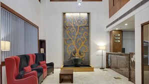 A lobby with a red and black sofa, a small table, a decorative wall with a tree design, and a reception desk.