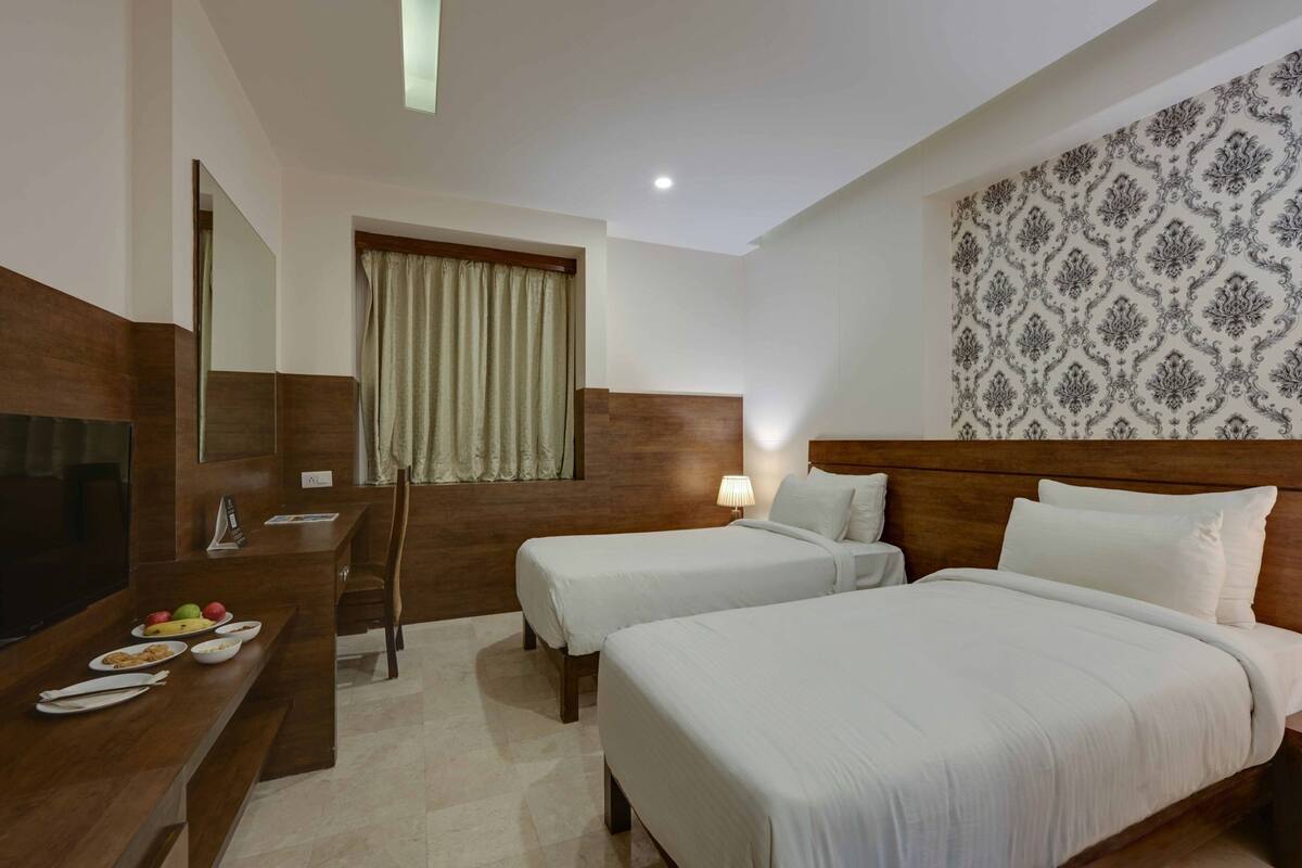 Een hotelkamer met twee bedden, een bureau met televisie en een eethoek met borden eten.