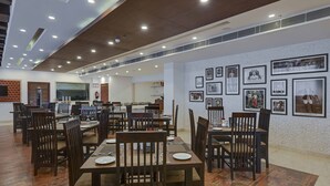 A spacious dining area with wooden tables and chairs, a kitchen in the background, and framed pictures on the walls.
