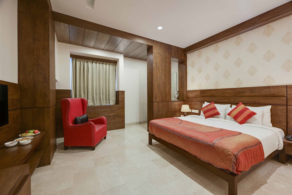 Une chambre d’hôtel avec un lit, un fauteuil rouge, une table de chevet et une fenêtre avec des rideaux.
