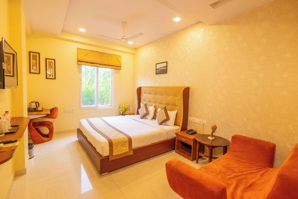 A hotel room with a large bed, a desk with a chair, a small table, and a sofa.