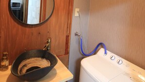 A bathroom with a wooden vanity, a round mirror, a sink, and a white washing machine.