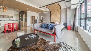 Ett modernt hotellrum med en soffa, en matplats med röda pallar, ett köksutrymme och stora fönster som släpper in naturligt ljus.