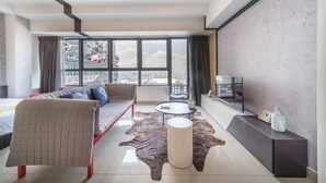 Ett modernt hotellrum med ett stort fönster, en soffa, ett soffbord, en tv och en matta i läder.