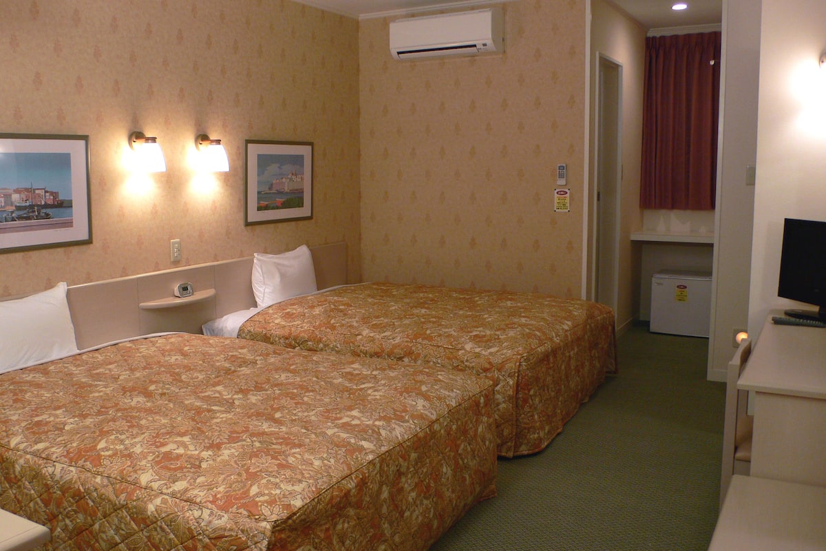 A hotel room with two beds, a small desk, a TV, and a mini-fridge.