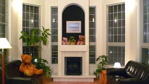 A living room with a fireplace, two black leather sofas, a large teddy bear, and two potted plants. - Family Lodge Hatagoya Kanazawa Uchinada (Uchinada)