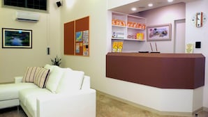A reception area with a white couch, a brown reception desk, and shelves with orange items. - Family Lodge Hatagoya Takamatsu (Takamatsu)
