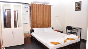 A hotel room with a bed, a desk, a chair, a wardrobe, and an air conditioning unit. - KPA Grand Palace (Sriperumbudur)