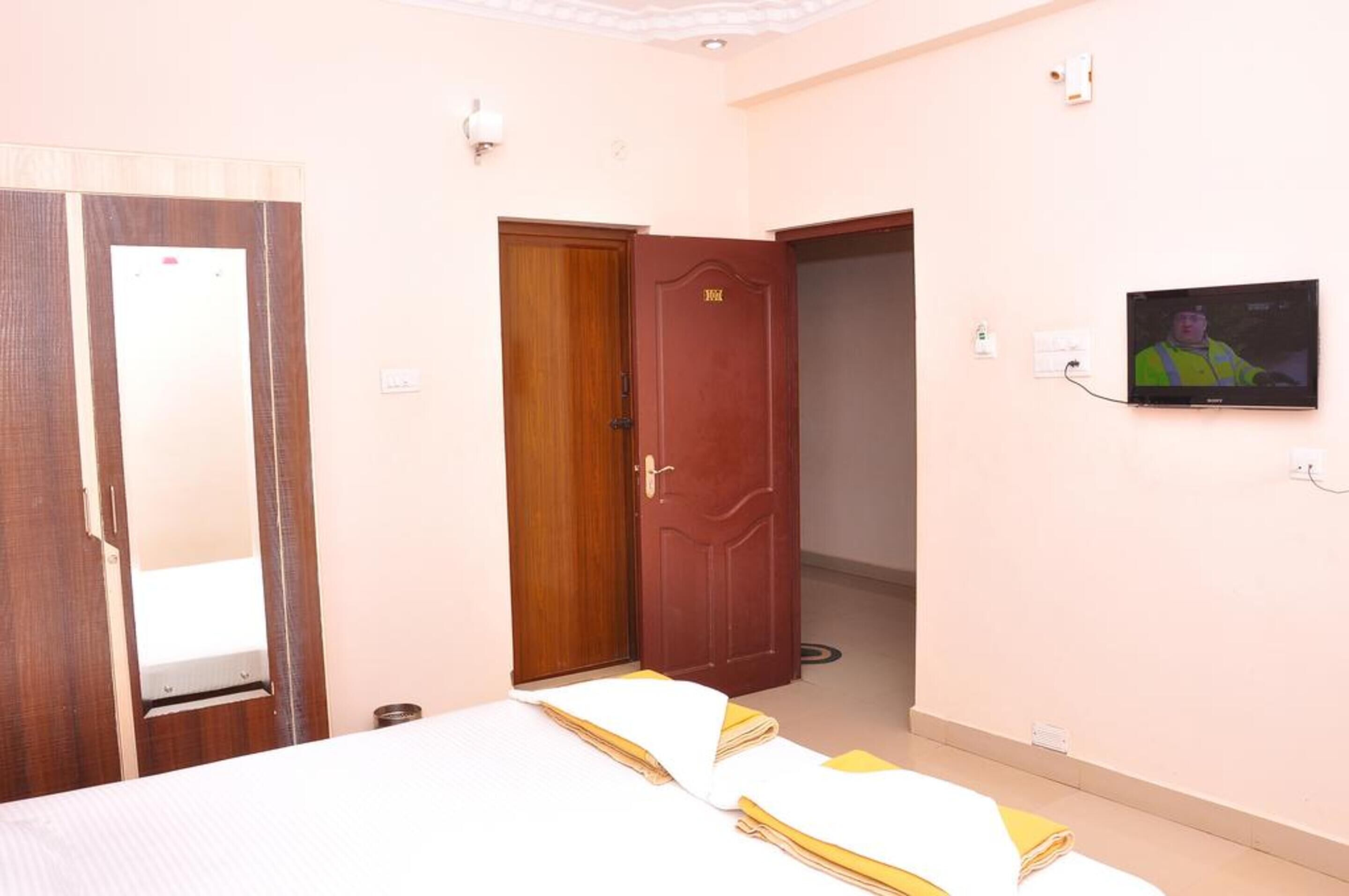 Habitación de hotel con una cama, una puerta de madera, un televisor y un espejo.