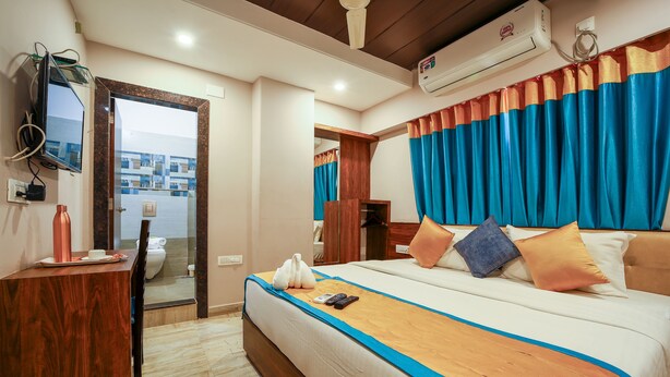 A hotel room with a bed, a TV, an air conditioner, and a view of the outside.