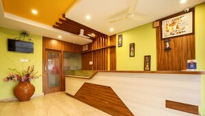 A reception area with a wooden reception desk, a flat-screen TV mounted on the wall, and a ceiling fan.