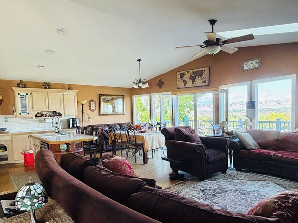 A spacious living area with a dining table, leather sofas, and a large window with a mountain view. - Million Dollar View, seasonal pool, close activities w/in 2-5 miles. Yes, pets! (Grand Junction)