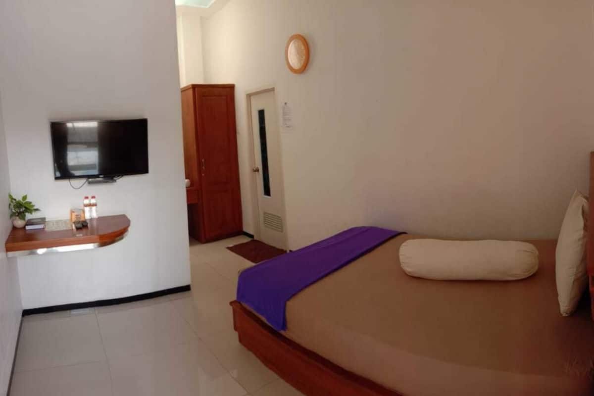 A hotel room with a bed, a TV, a desk, and a door.