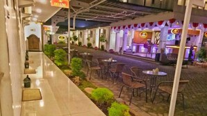 An outdoor seating area with tables and chairs, a pathway, and a restaurant in the background. - Sultan Guest House & Resto Tulungagung (Tulungagung)