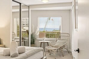 A modern bedroom with a balcony, a white sofa, a wicker chair, and a small table. - Apartment R113 - a secluded beachside retreat! (Scarborough)