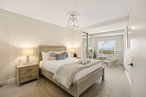 A bedroom with a wooden bed, bedside tables, a nightstand, a ceiling light fixture, and a view of a balcony with outdoor furniture. - Apartment R113 - a secluded beachside retreat! (Scarborough)