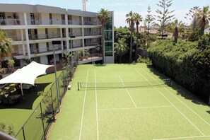 A tennis court surrounded by a fence, with a multi-story building in the background. - Apartment R113 - a secluded beachside retreat! (Scarborough)