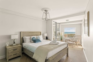 A bedroom with a bed, bedside tables, a lamp, a chair, a window with a view, and a ceiling light fixture. - Apartment R113 - a secluded beachside retreat! (Scarborough)