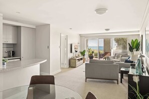 A modern living room with a glass dining table, a sofa, and a TV.