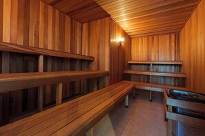A sauna with wooden benches and walls, a bench with a tray, and a light fixture on the ceiling. - Apartment R113 - a secluded beachside retreat! (Scarborough)