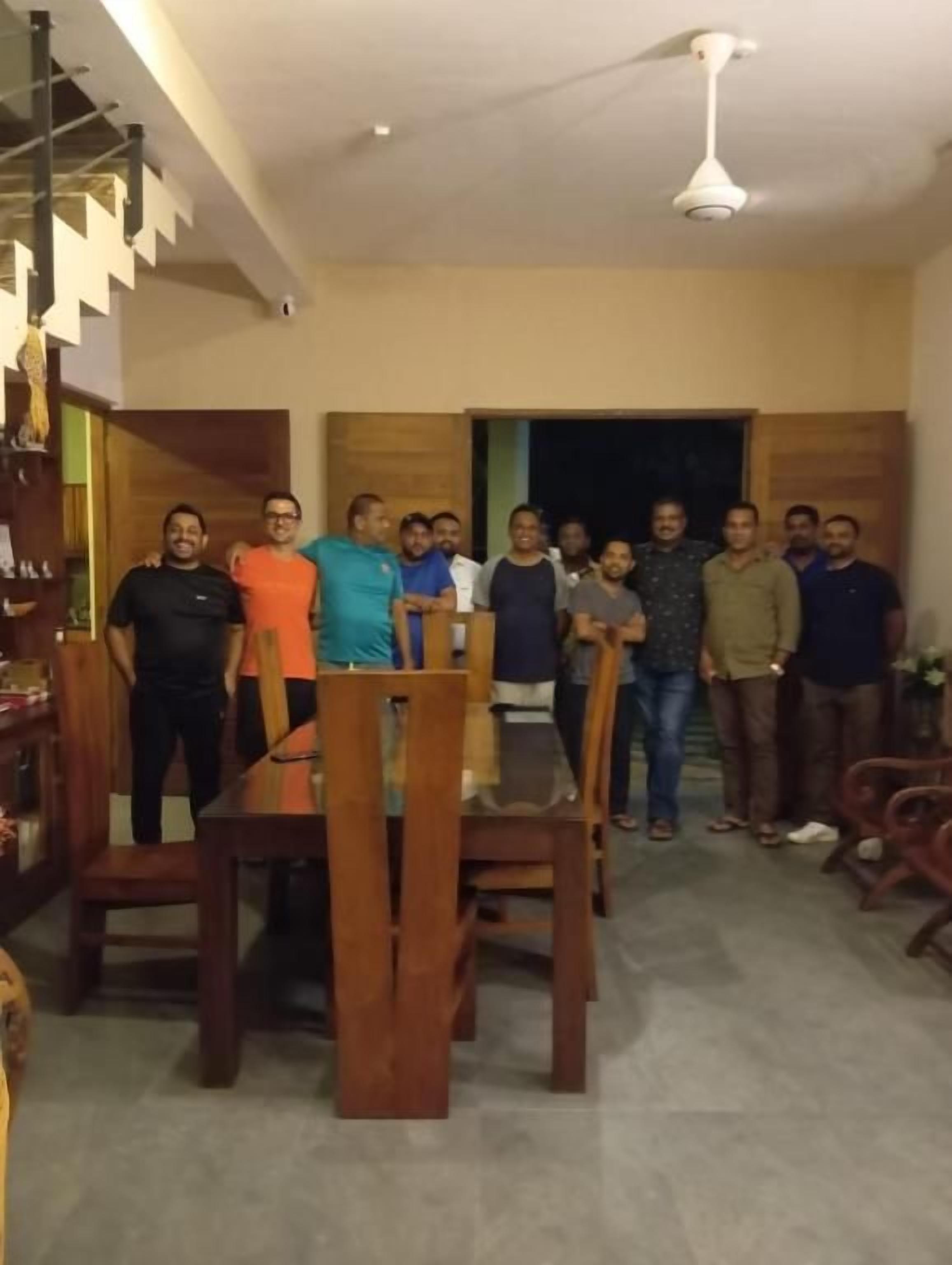 A group of people standing in a room with a dining table and chairs, a staircase, and a ceiling fan.