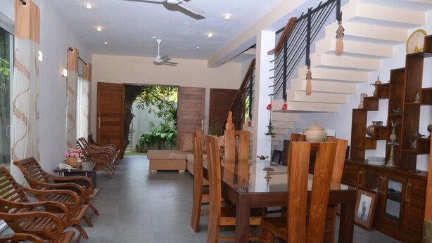 A dining area with wooden chairs and a table, a staircase with a railing, and a view of greenery outside. - Kelaniya Heritage (Kiribathgoda)