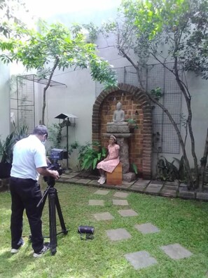 A garden with a statue, a camera on a tripod, and a person in a pink dress. - Kelaniya Heritage (Kiribathgoda)