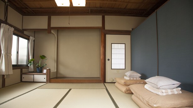 A traditional Japanese room with tatami flooring, a shoji screen door, and a futon bed with pillows. - Guest house tokonoma - Hostel (Kamijima)