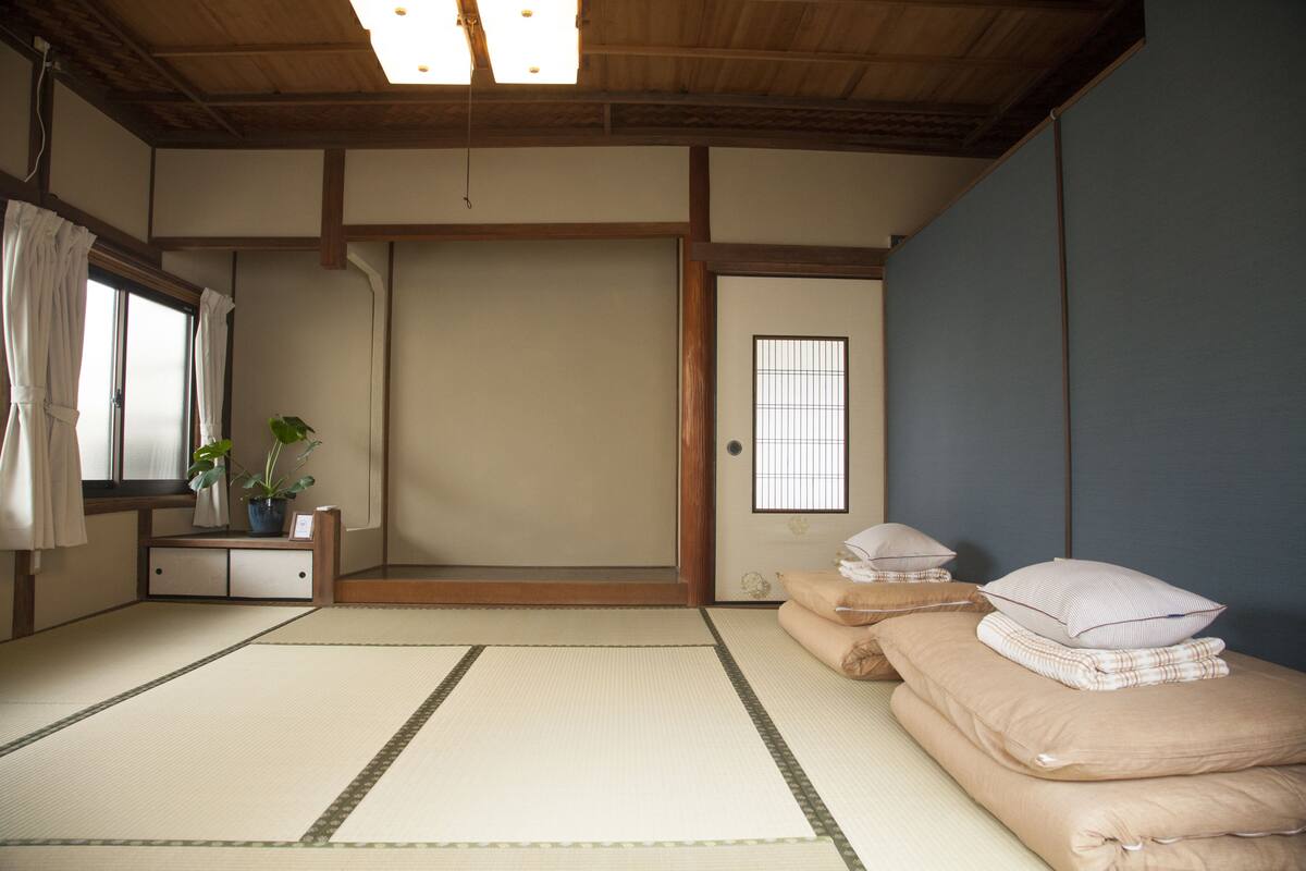 A traditional Japanese room with tatami flooring, a shoji screen door, and a futon bed with pillows.