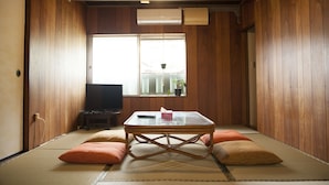 A traditional tatami room with a low table, cushions, a television, and a window with a view of the outside. - Guest house tokonoma - Hostel (Kamijima)