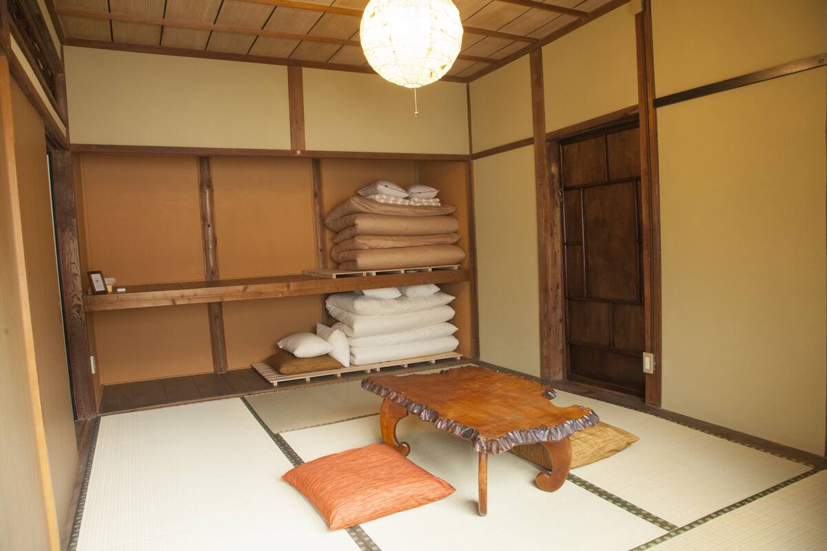 A traditional Japanese room with tatami flooring, a wooden table, and a shelf with folded textiles.