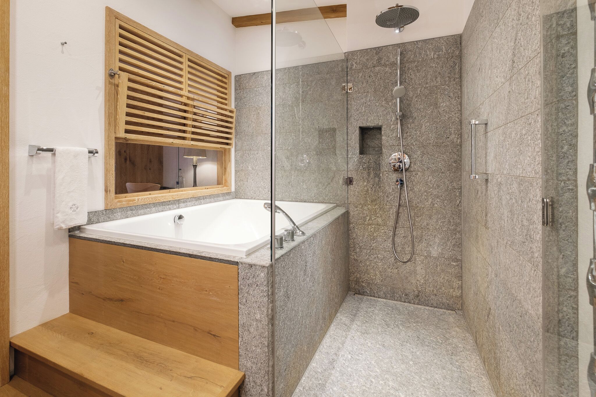 Een moderne badkamer met een vrijstaand bad, een douche met glazen wanden en een houten bankje.