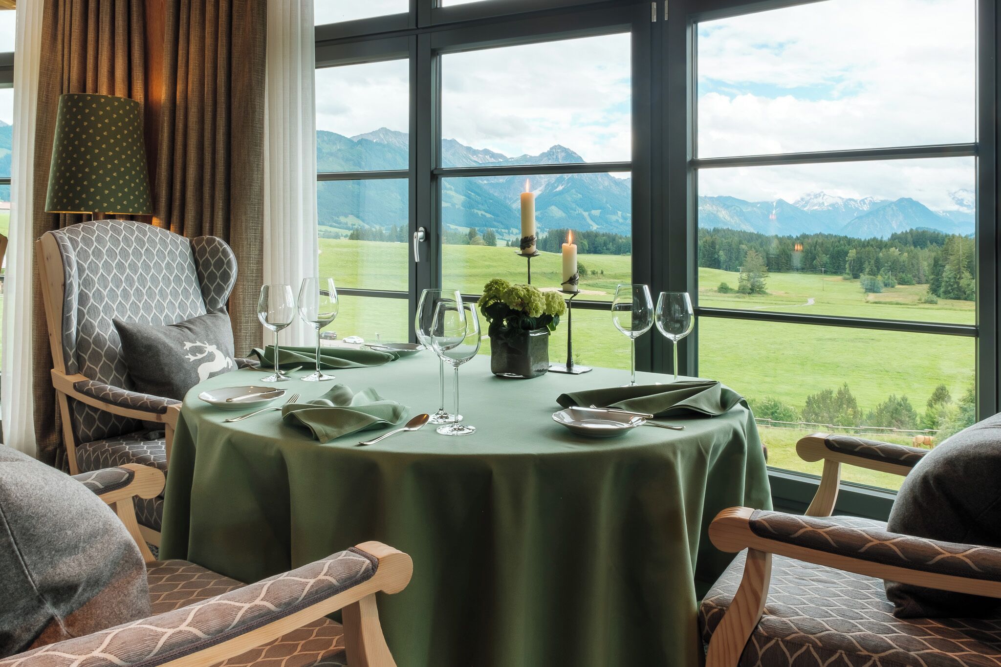 A dining table set for two with a view of mountains through large windows.