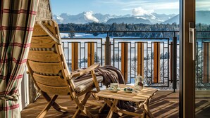 A wooden deck with a chair and table, overlooking a snowy landscape with mountains. - Sonnenalp Resort (Ofterschwang)