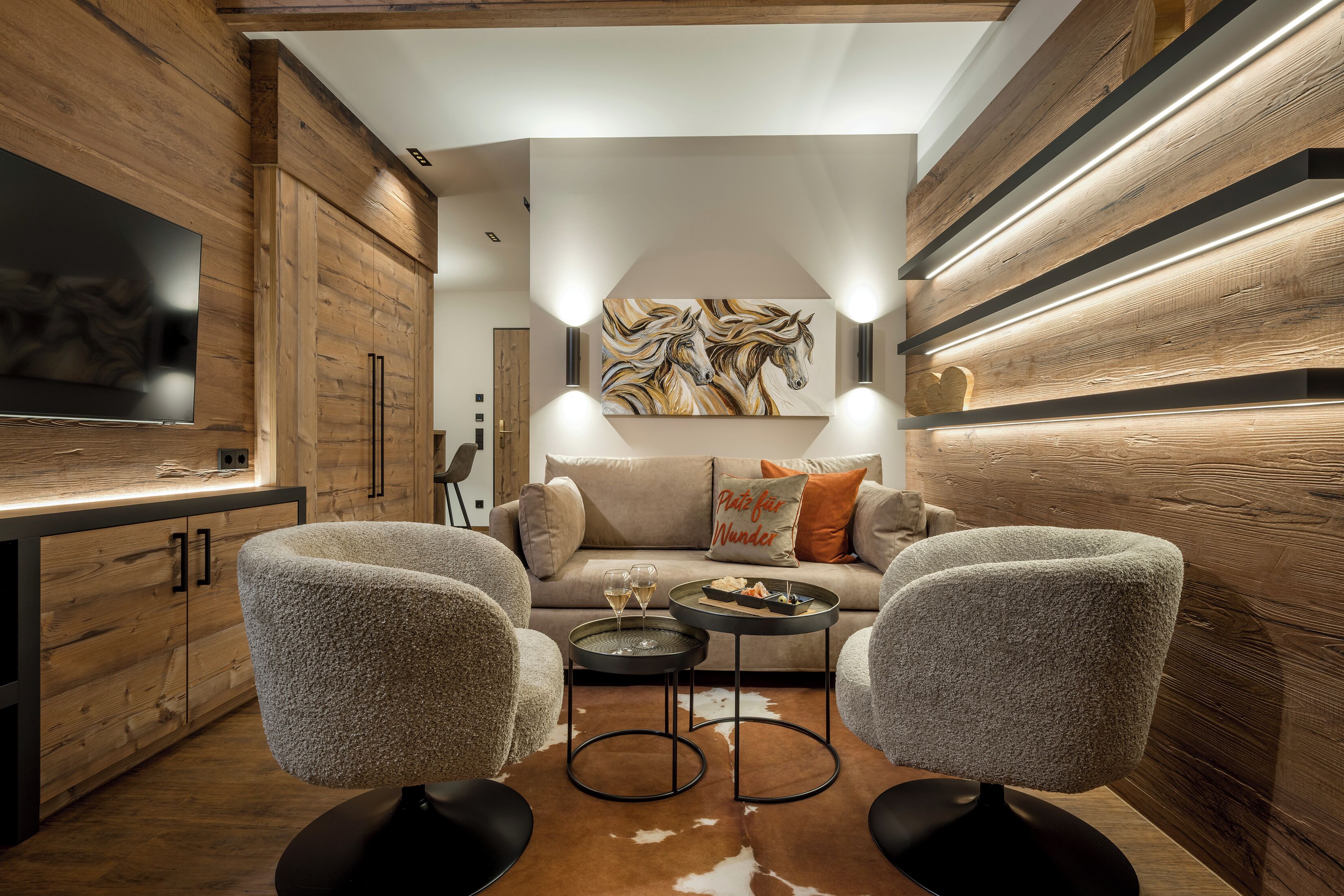 Una sala de estar moderna con un sofá, dos sillones, una mesa de centro y un televisor de pantalla plana montado en la pared.