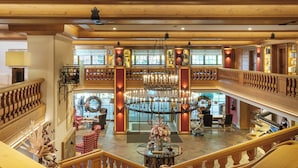 A multi-level hotel lobby with a grand chandelier, wooden railings, and a central seating area. - Sonnenalp Resort (Ofterschwang)