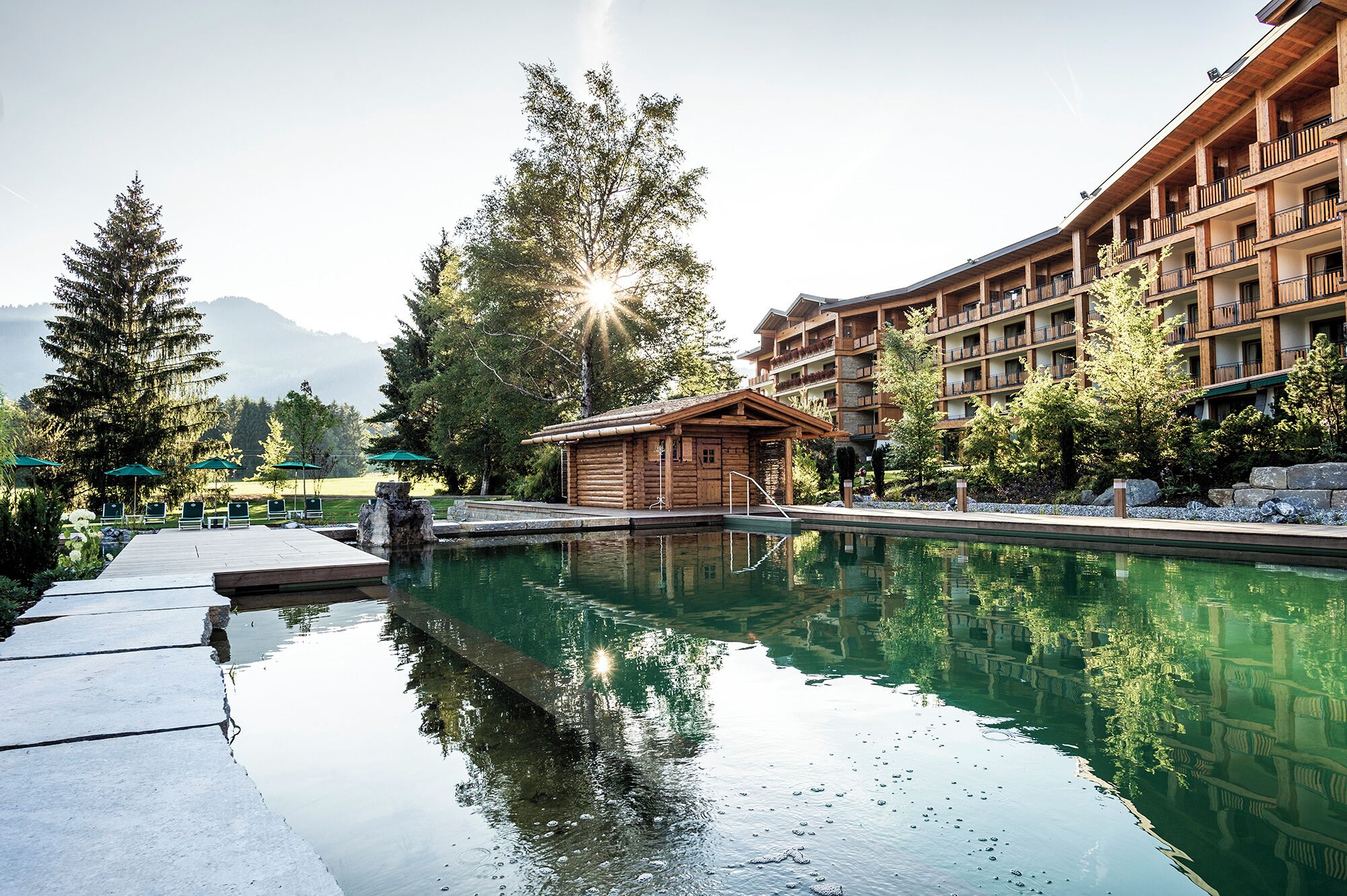 A resort with a swimming pool, wooden cabins, and a mountain backdrop.